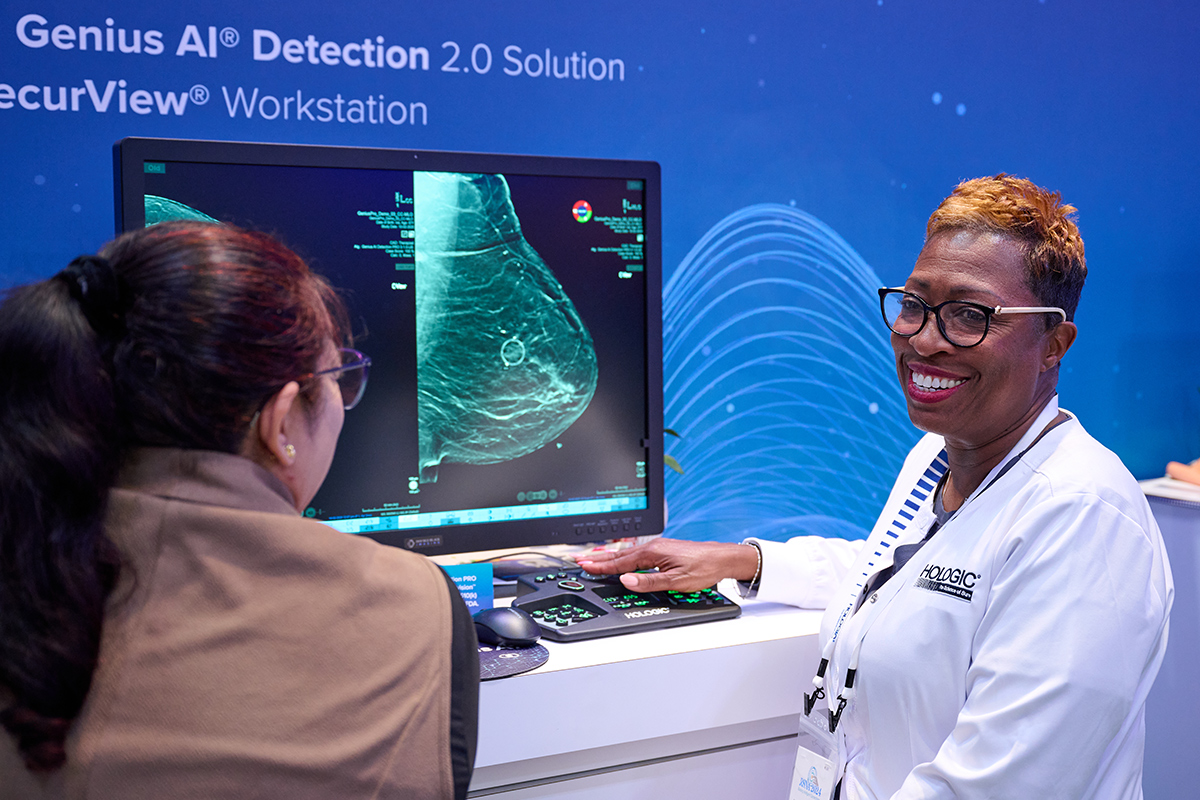 Two individuals stand in front of screen displaying mammogram image.