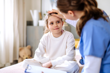 Child sits on hospital bed next to nurse.