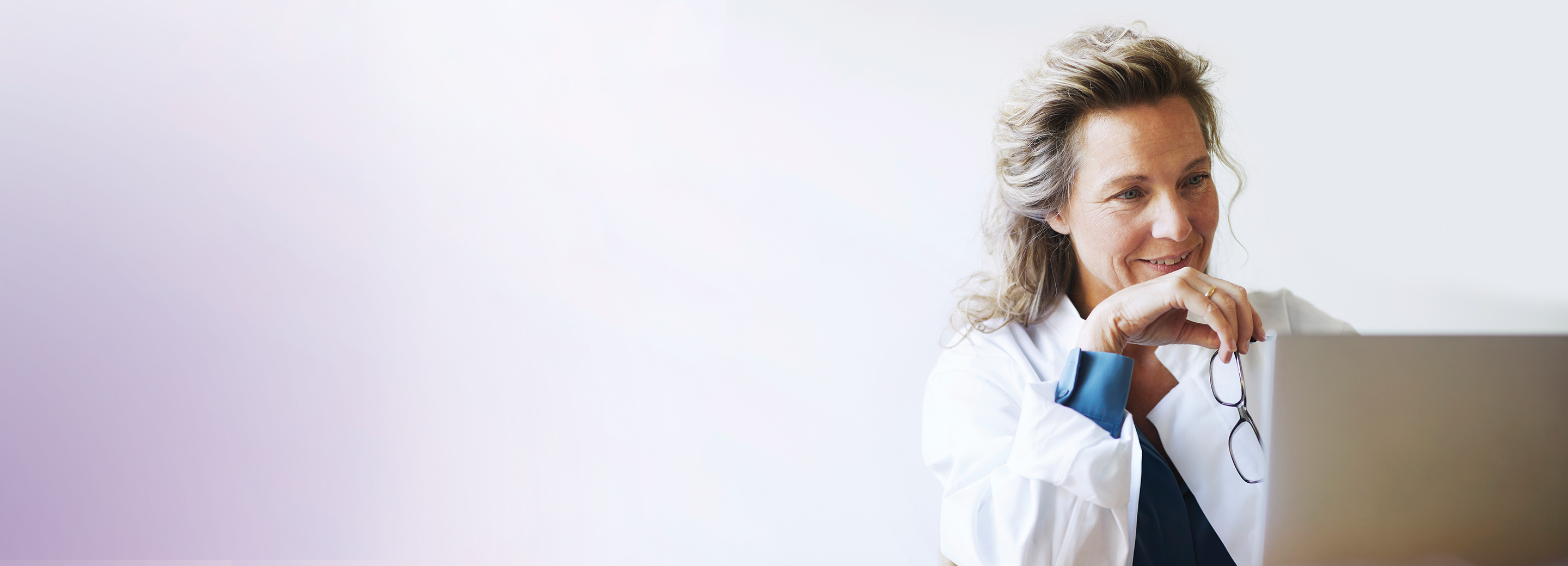 Doctor holding eyeglasses and looking at laptop