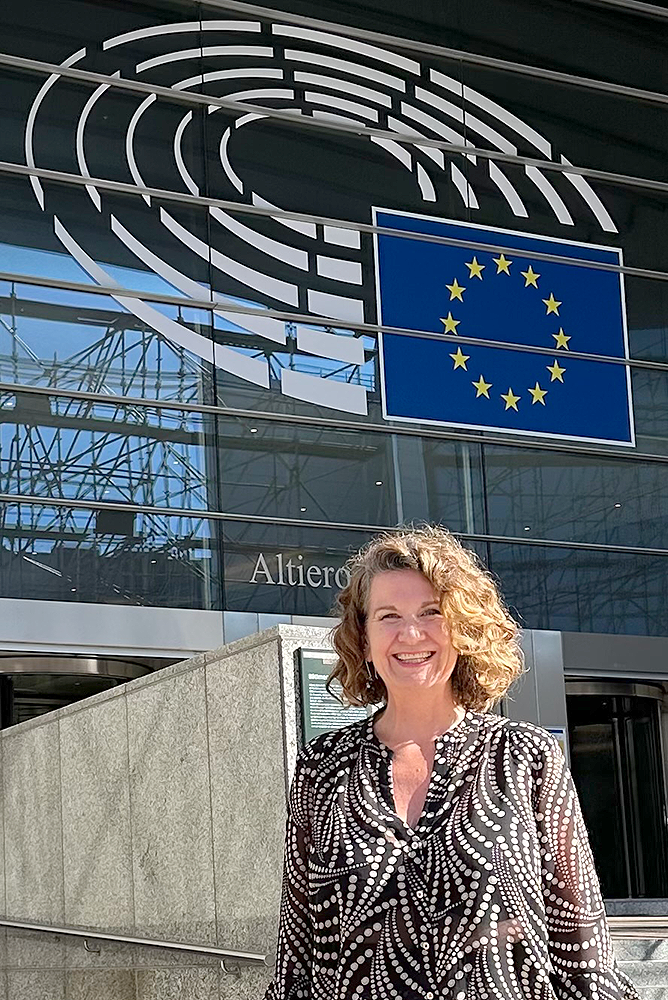 Woman stands outside a glass building with flag.