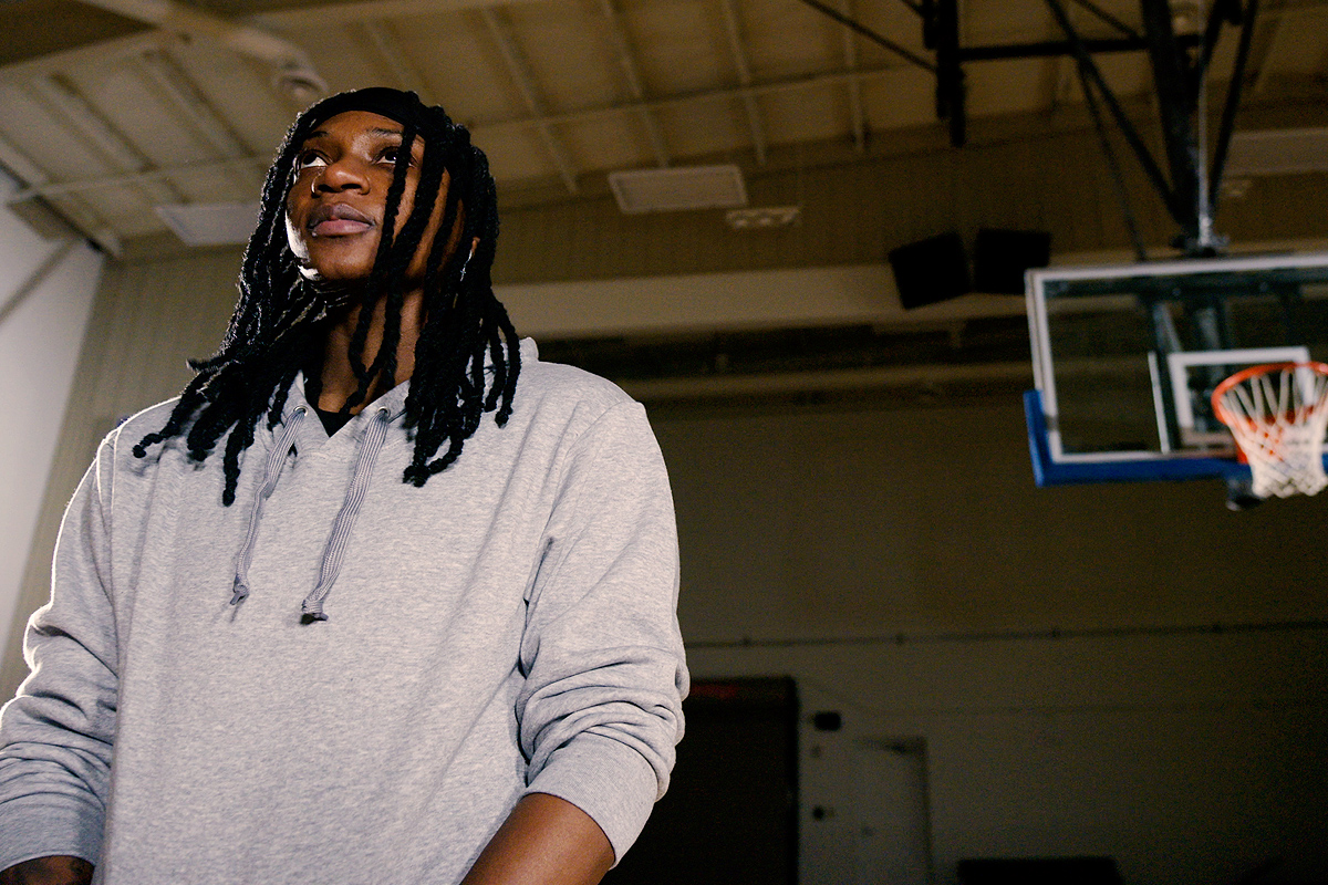 Woman in grey sweatshirt stands next to basketball hoop.