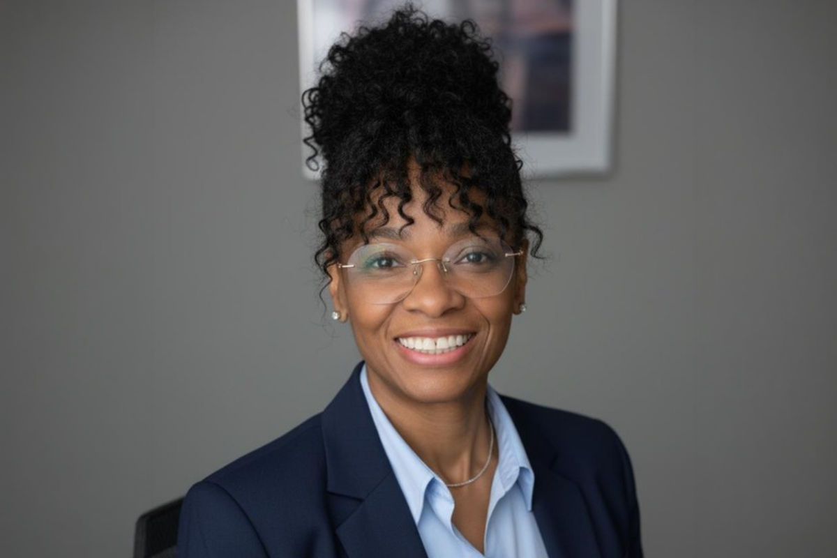 Woman with glasses wearing a light blue shirt and blue jacket smiling.