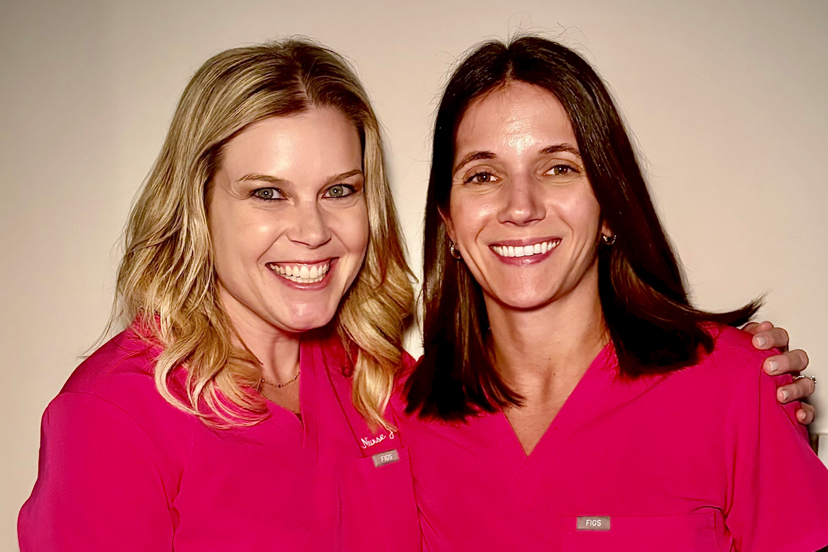 Two women smile in pink medical scrubs.