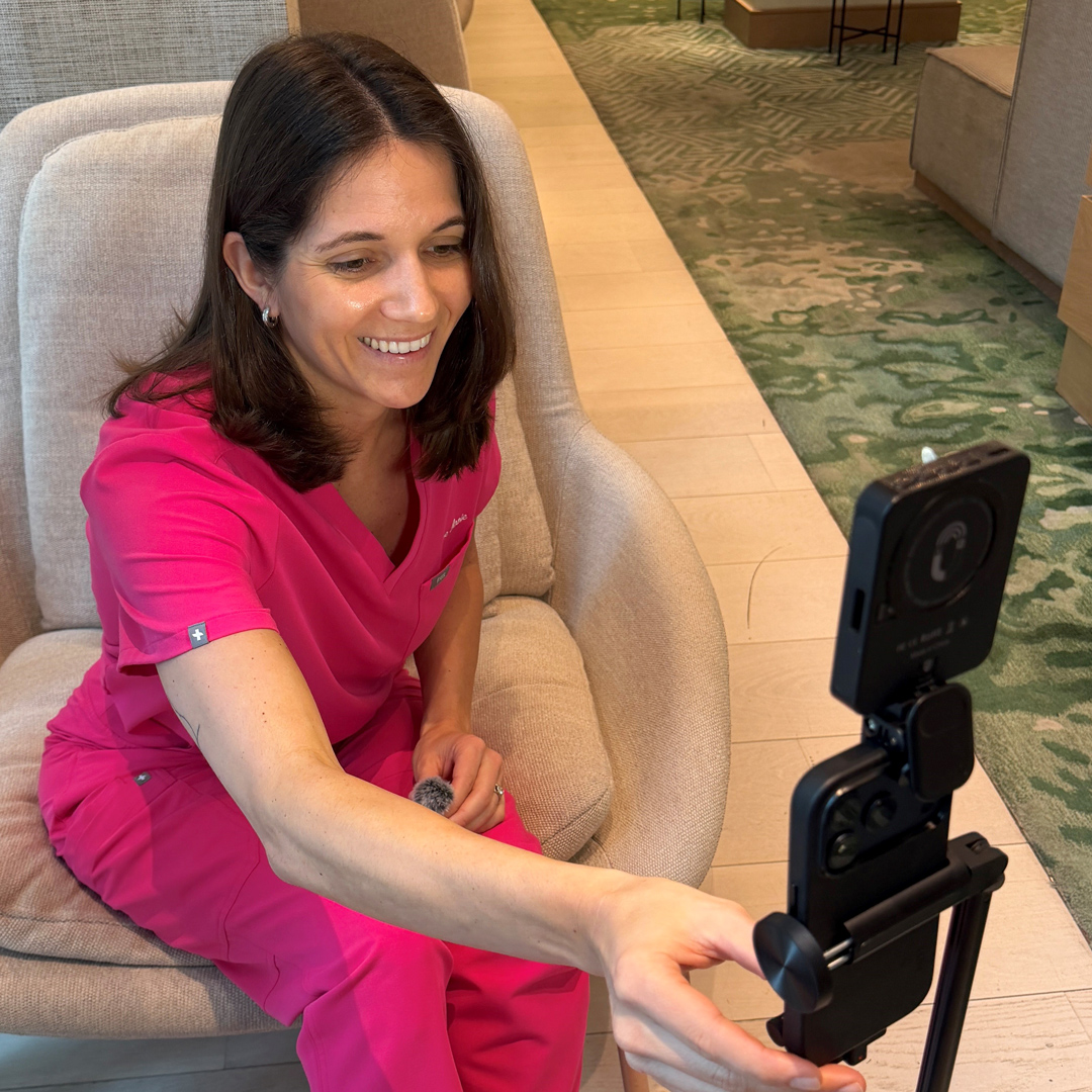 Woman in pink medical scrubs recording video on her phone.