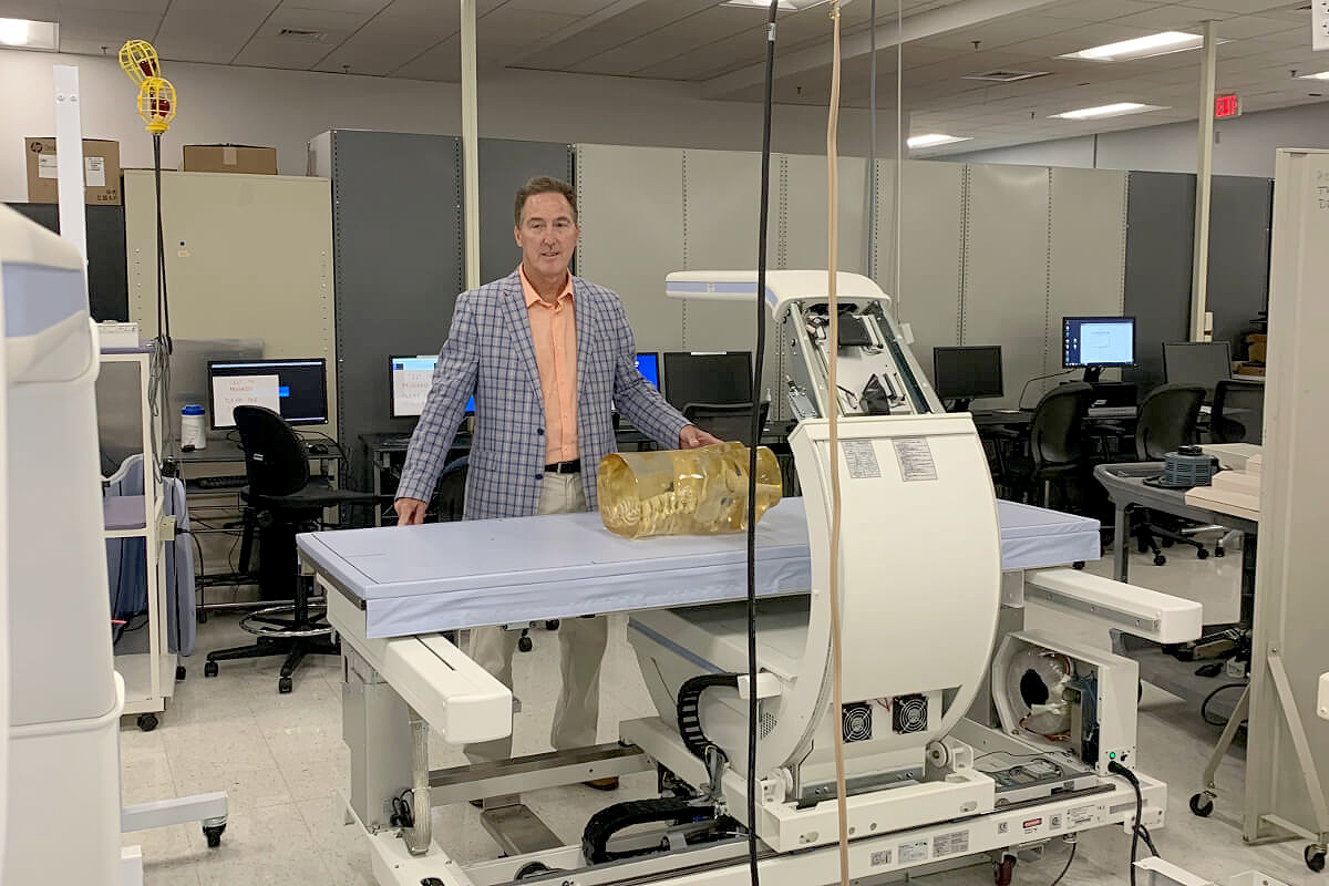 Man in blue jacket stand behind a medical device.