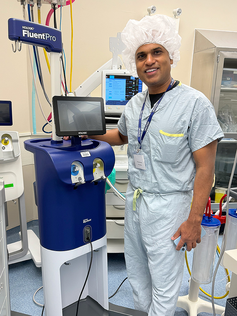 Man in medical scrubs stands next to medical device. 