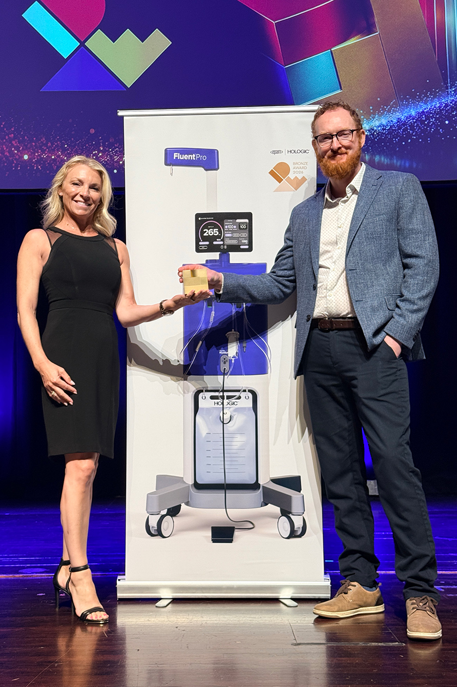 A man presents a bronze award trophy to a woman on stage beside a Hologic FluentPro banner.
