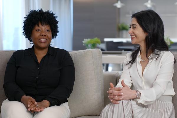 Two women sitting and speaking in a home environment.