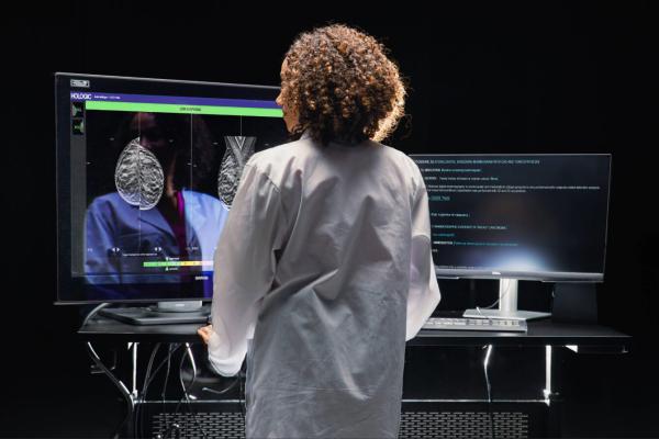 Woman working at desk with 2 monitors in dark setting.