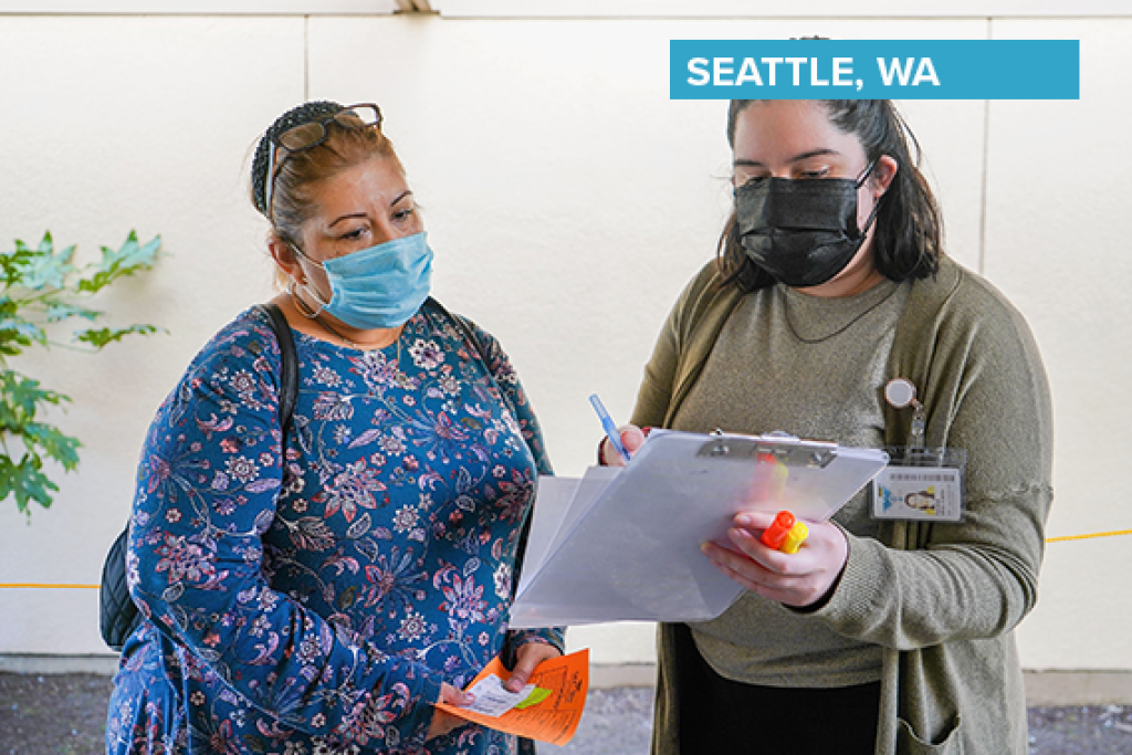 Two masked women speaking in an office setting.