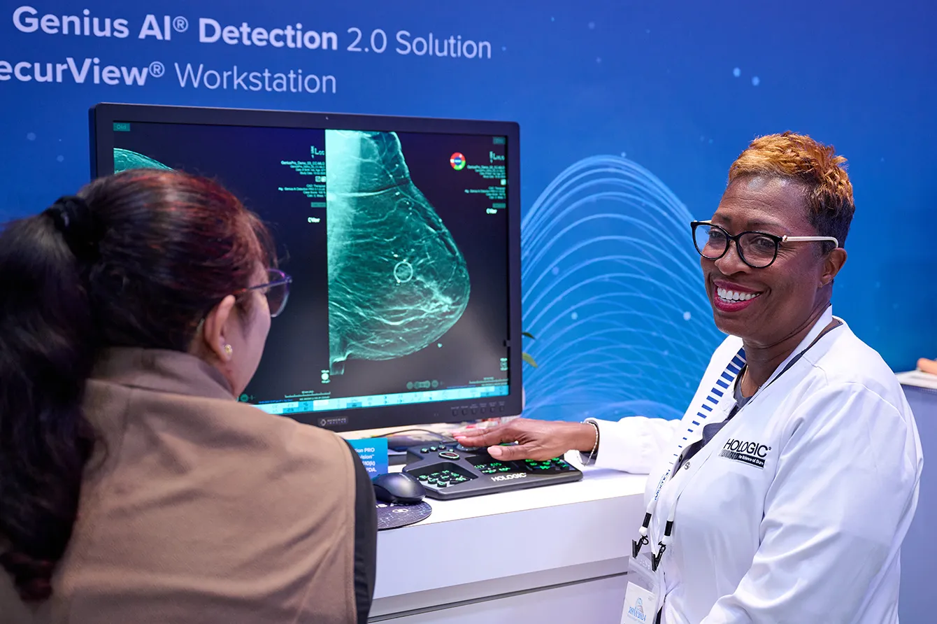Two individuals stand in front of screen displaying mammogram image.