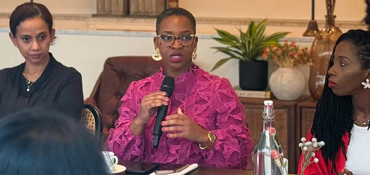 Three women sit at a table with one speaking into a microphone.