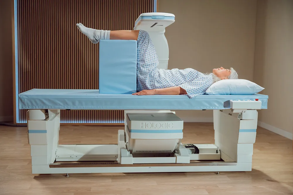 Woman laying on exam table with medical device scanning her in exam room setting.