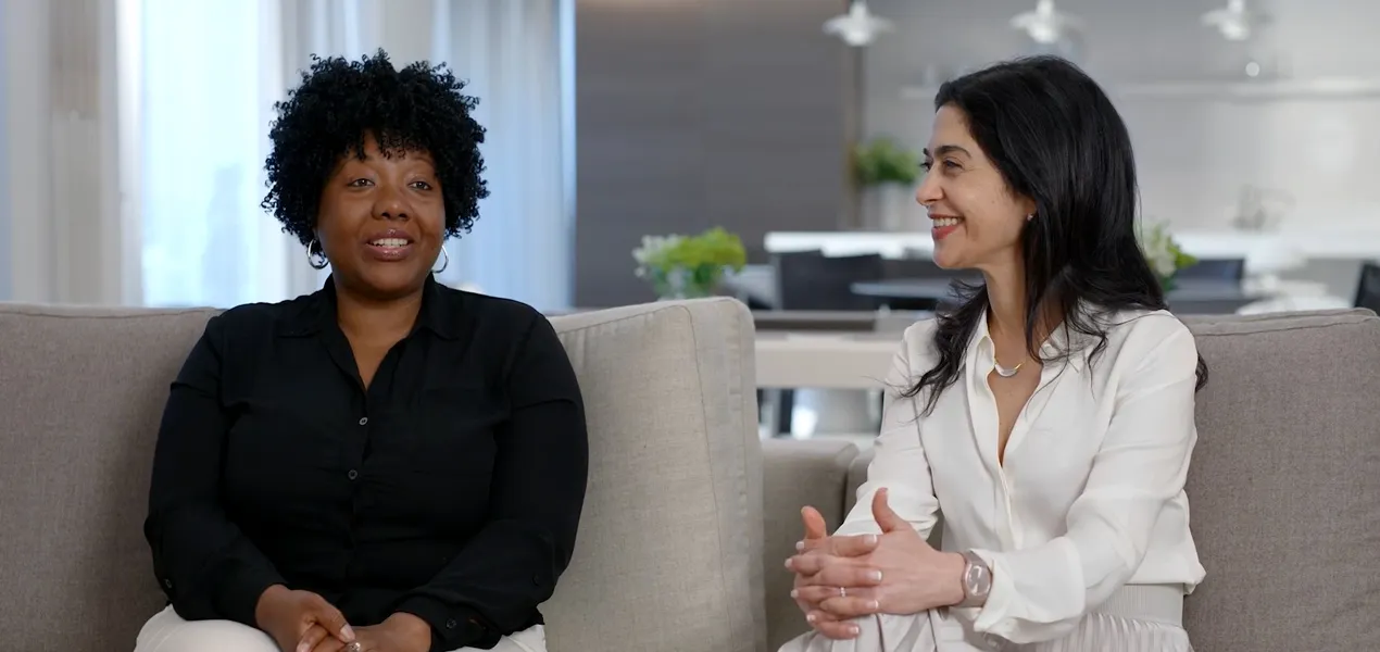 Two women sit on a couch having a conversation.