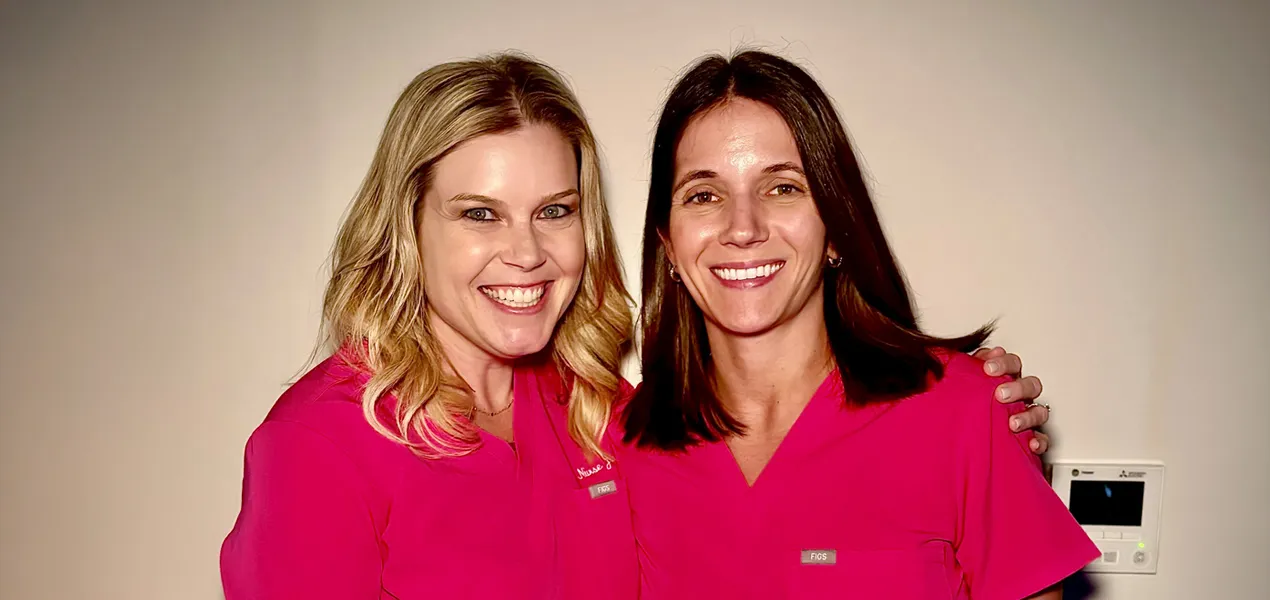 Two women smile in pink medical scrubs.