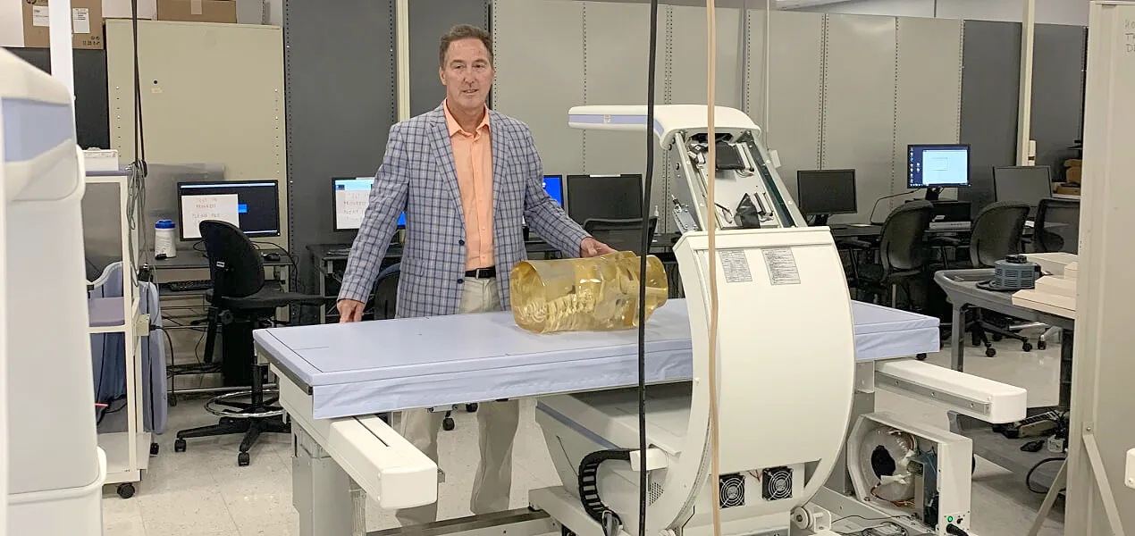 Man in blue jacket stands behind a medical device.