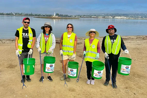 Group photo of volunteers wearing bright vests and holding buckets near beach line.