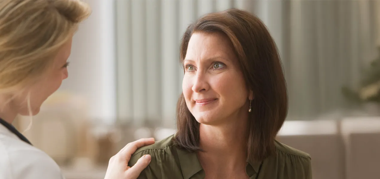Woman with brown hair smiles while talking to doctor.