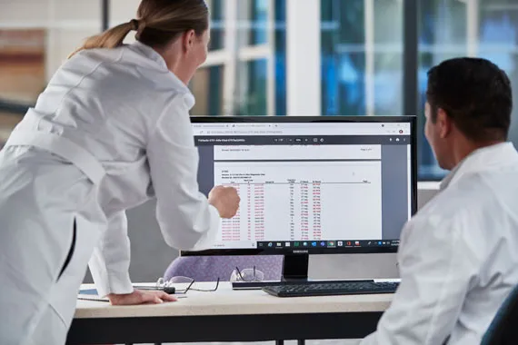 Two healthcare providers at a desk looking at data on a display monitor