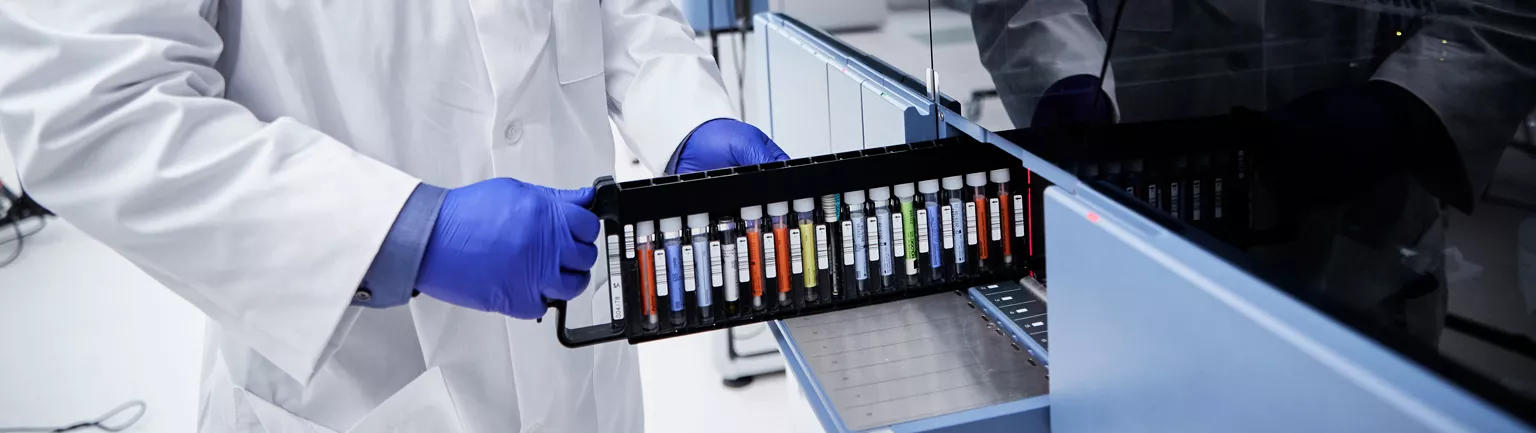 Technician loads tray of vials in machine in lab setting.