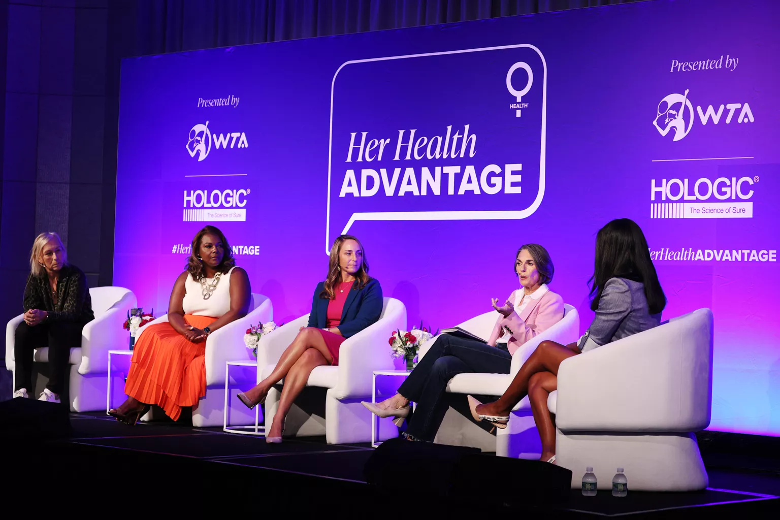 Group photo with Dr. Susan Harvey, WTA legend Martina Navratilova and WTA athletes Sloane Stephens and Madison Keys sitting on stage speaking.